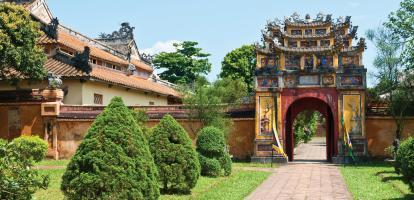 Coloured gate surrounded by an orange wall and gardens is the entry point to Hung To Temple in Hue's imperial city, Vietnam
