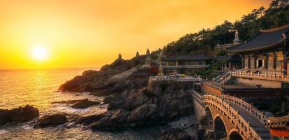 Sun setting over sea next to ornate temple and bridge in Busan
