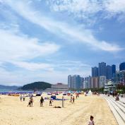 People walking along sandy beach with skyscrapers of Busan in background