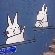 Street art on a blue wall of two cute bunnies in Ilhwa Mural village
