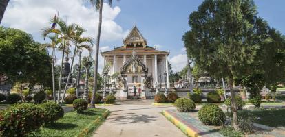 White buddhist temple with golden roof is surrounded by beautiful gardens in Battambang.