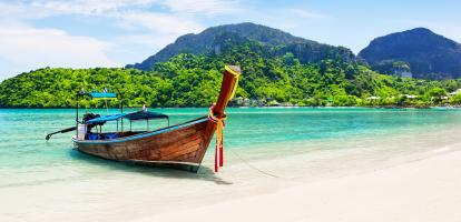 Boat on beautiful white sand in Koh Phi Phi with jungle-covered mountains in the background