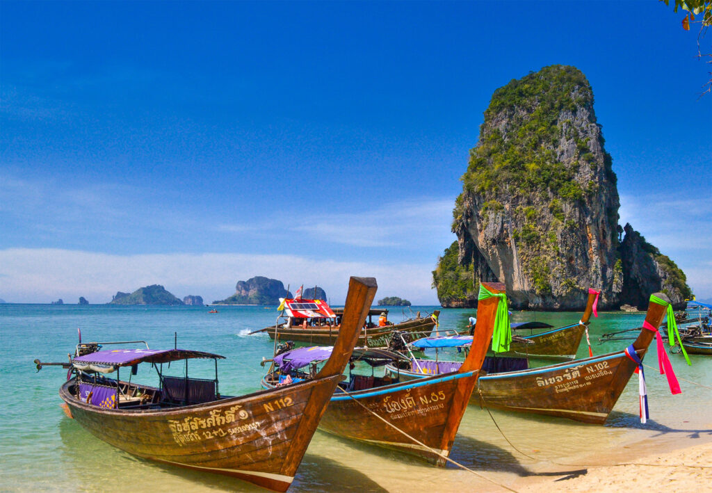 Boats parked in an azure beach surrounded by karst rock formations in Krabi, Thailand