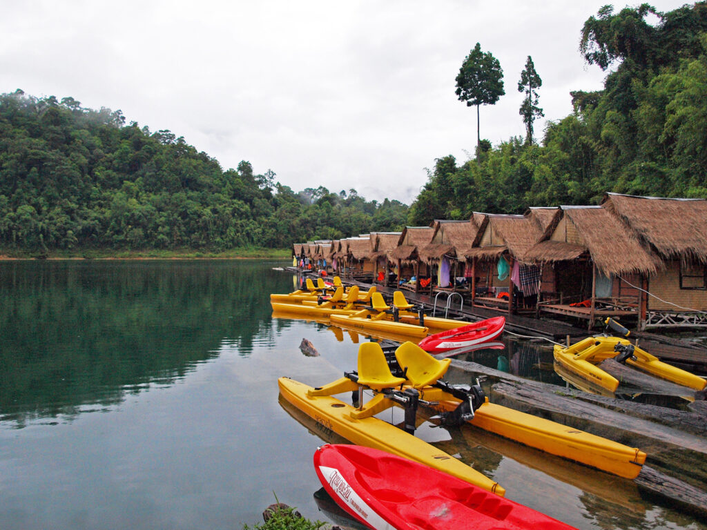 Kayaks and boats rest next to straw-thatched huts in Khao Sok national park, Thailand
