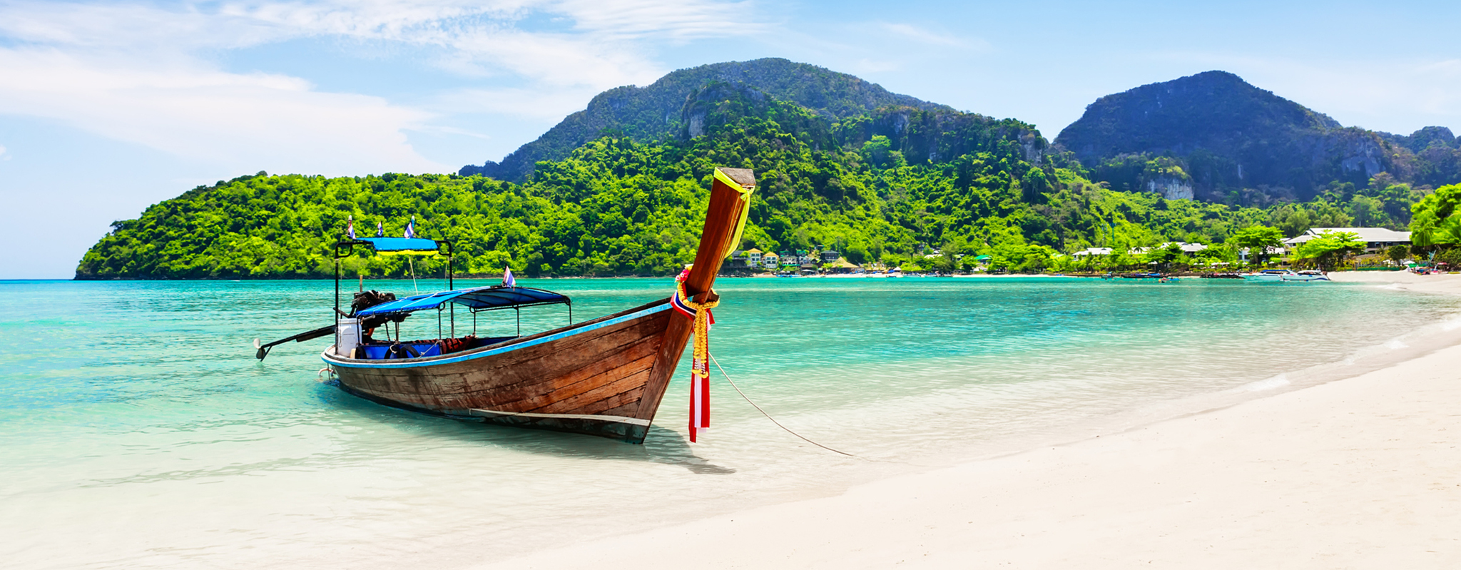 Boat on beautiful white sand in Koh Phi Phi with jungle-covered mountains in the background