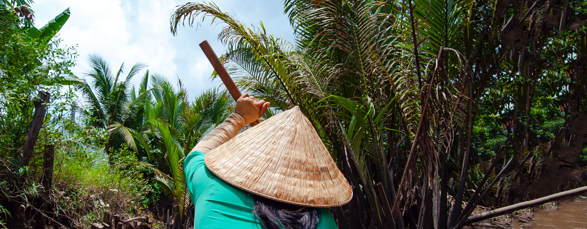 Woman wearing conical straw hat cruises in the Mekong Delta jungle