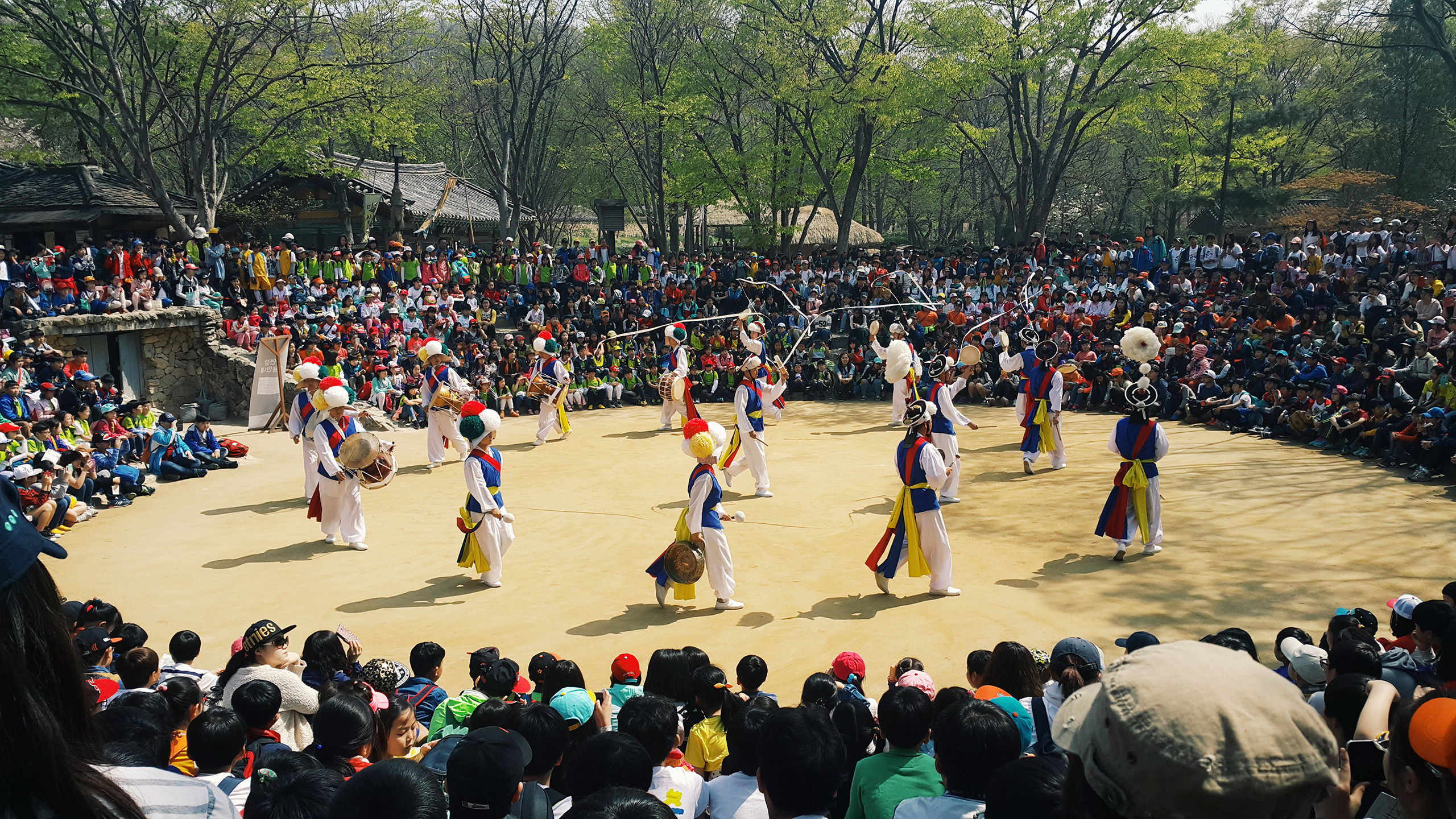 Dancers in traditional costume in circle surrounded by crowds of spectators