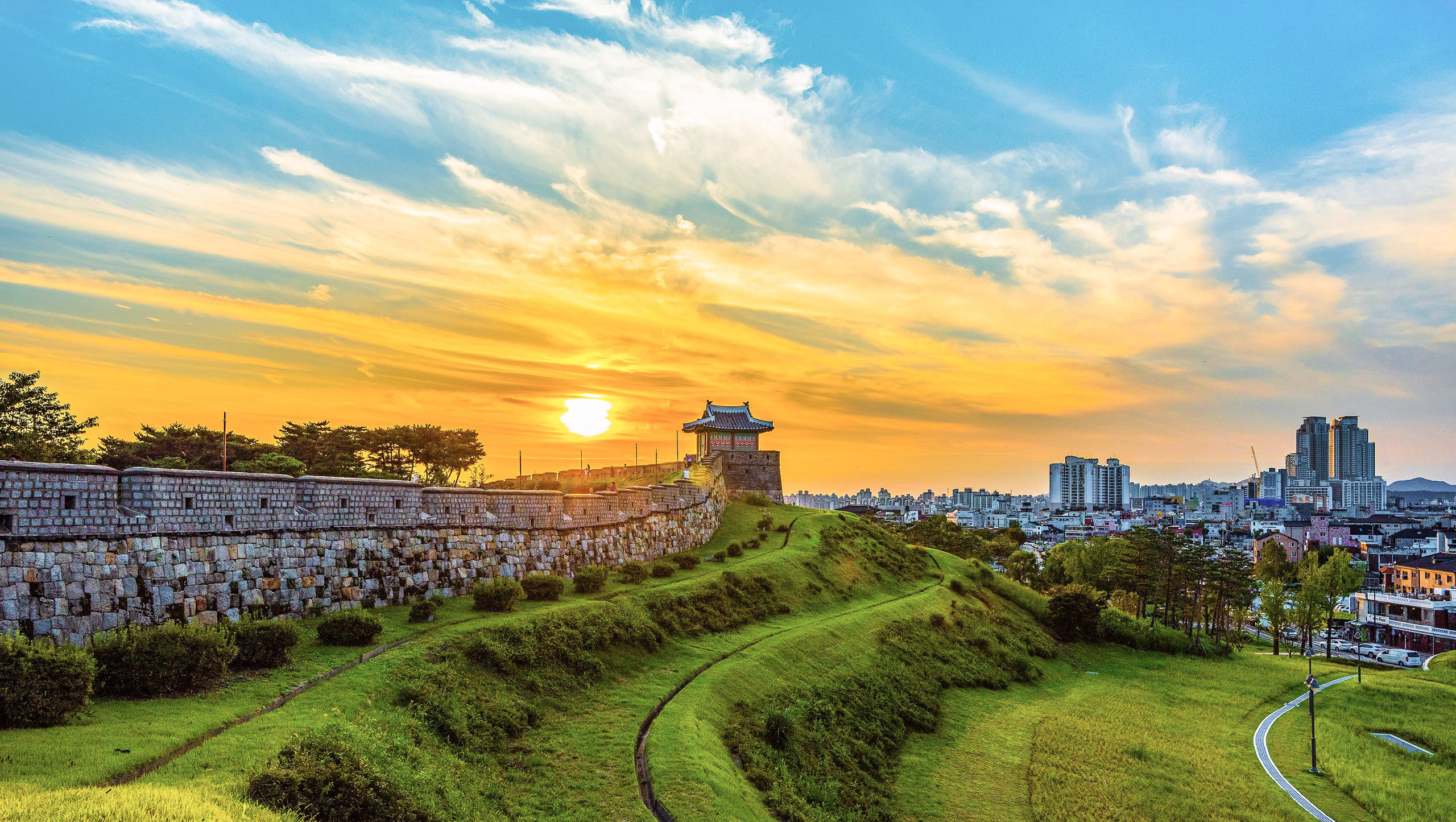 Suwon-fortress-at-sunset-city-skyline-hero.jpg Suwon fortress walls at sunset with city skyline in background