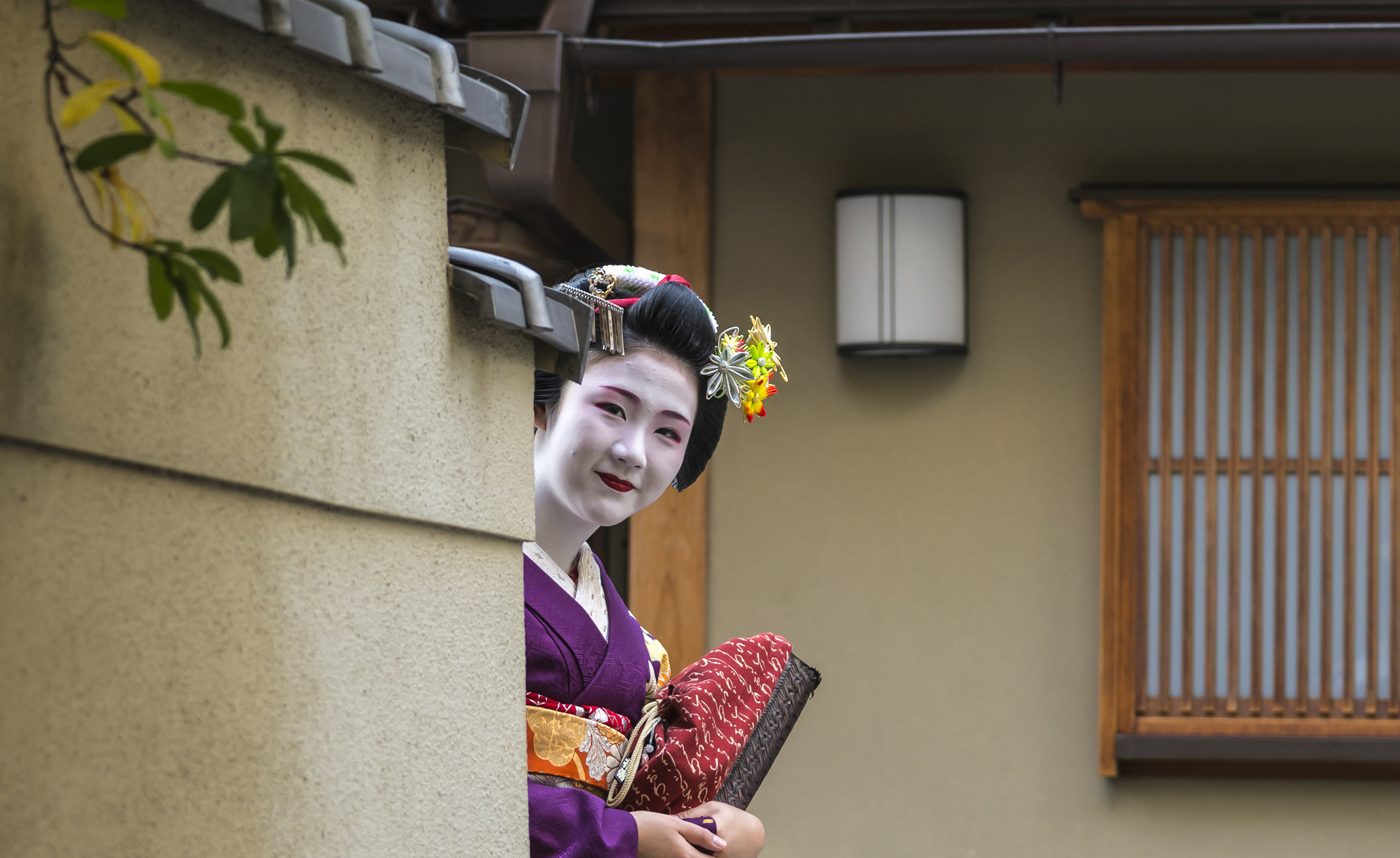 Geisha looking around corner and smiling at the camera