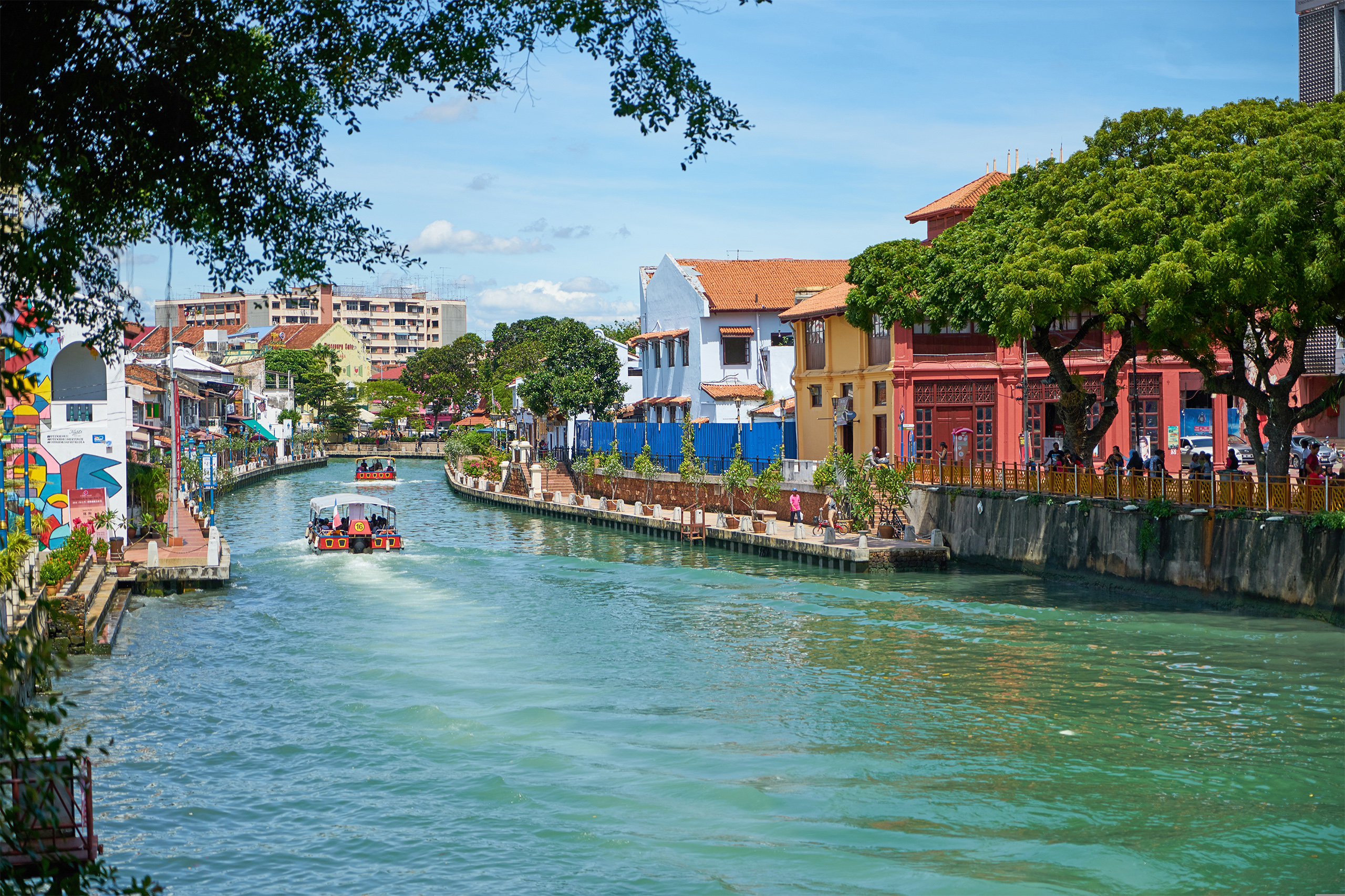 Boats with people navigate river traversing Malacca city in Malaysia