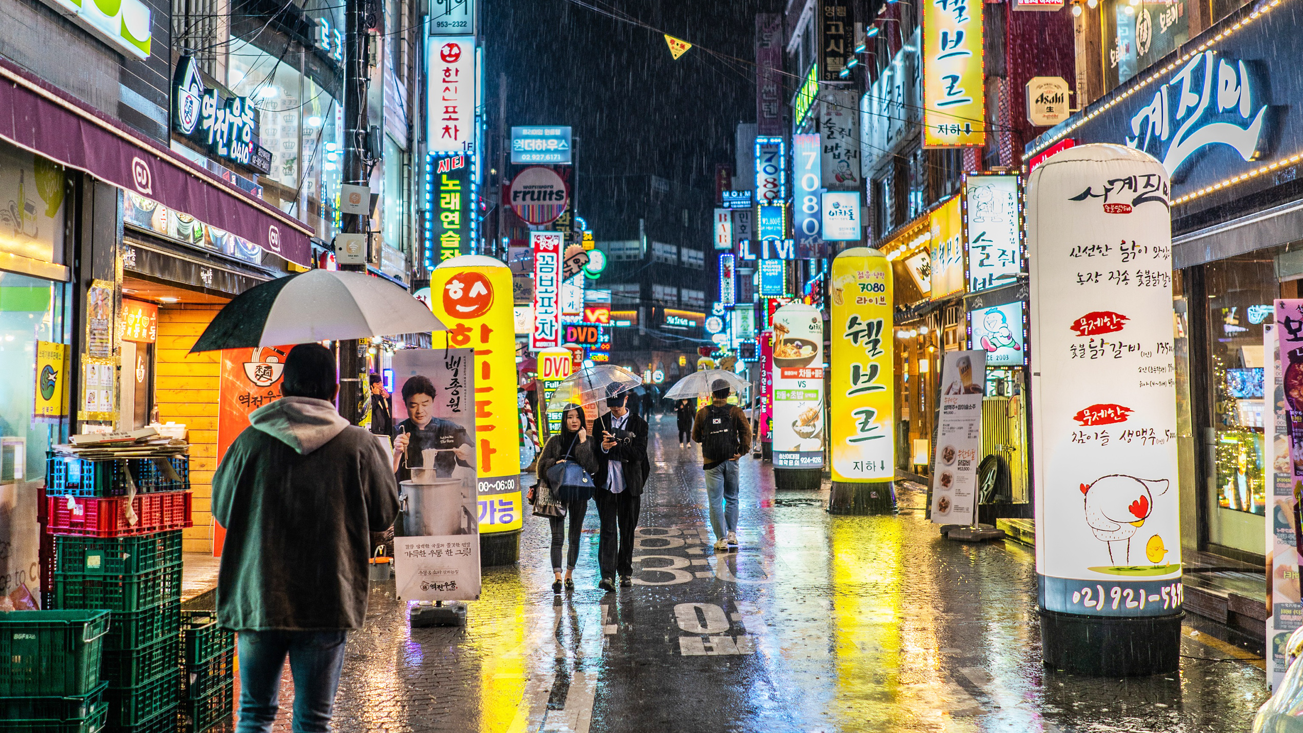Korean Wave Hero Image of a Korean city in the rain at night, with neon signs and people walkign