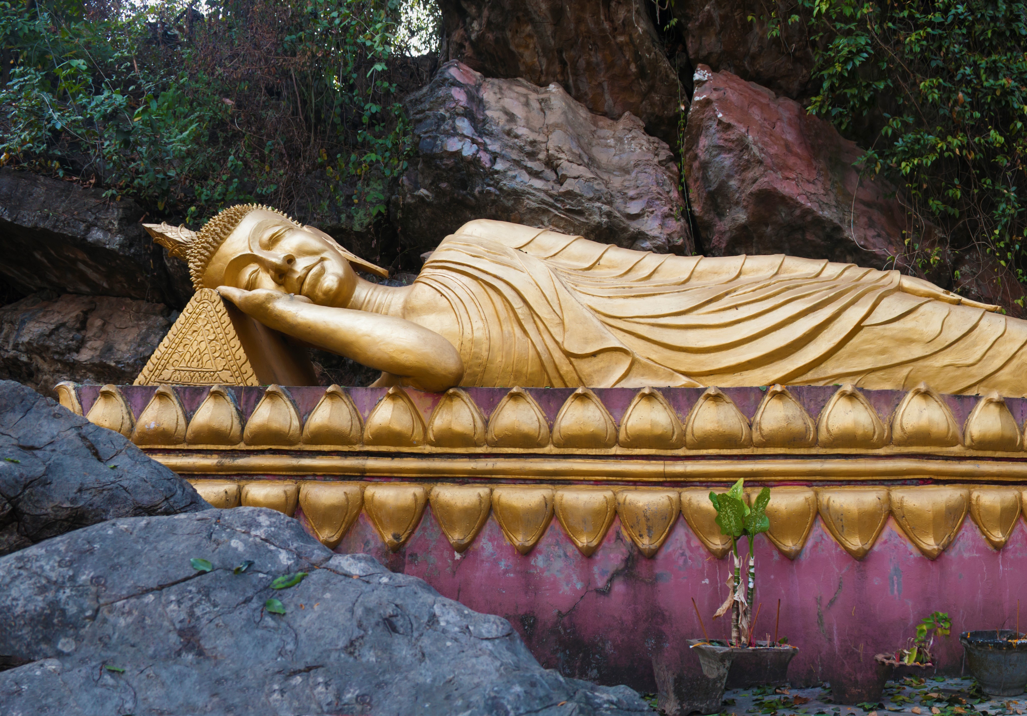 Luang Prabang Laos Reclining Buddha Reclining gold gilt buddha on purple platform surrounded by craggy rocks