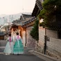 Back of two women wearing hanbok walking through the traditional style houses of Bukchon Hanok Village in Seoul, South Korea.