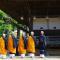 Monks in orange robes lined up to pray outside wooden temple