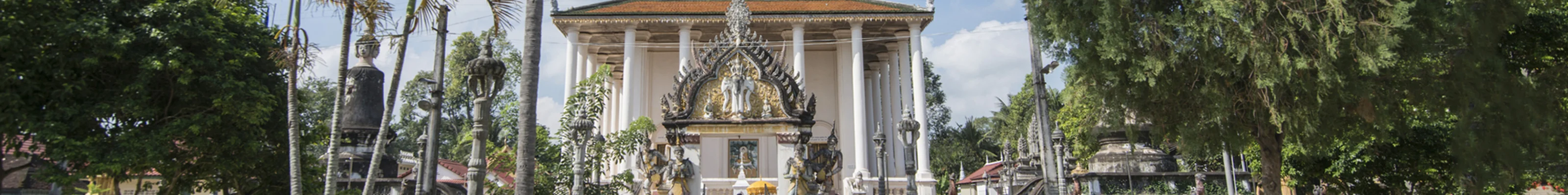 White buddhist temple with golden roof is surrounded by beautiful gardens in Battambang.