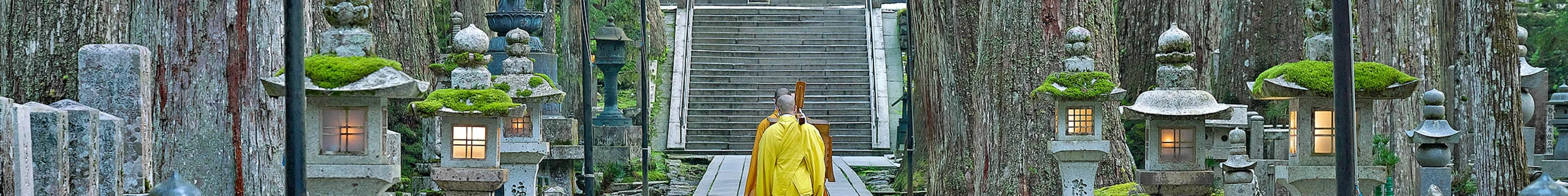 Monk in yellow clothes walking along pathway in Koya
