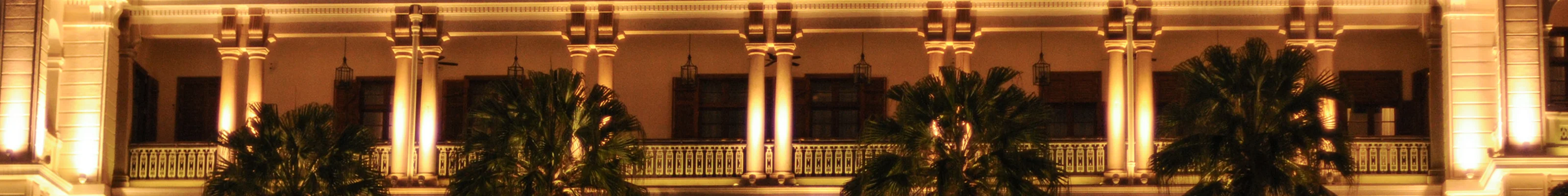 Heritage building lit up at night with palm trees outside 
