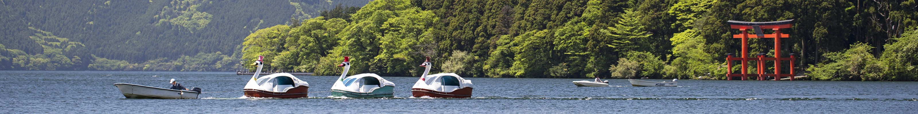 Small boat tows duck floaters in with Mount Fuji in the background in Lake Ashi, in the Hakone area of Japan