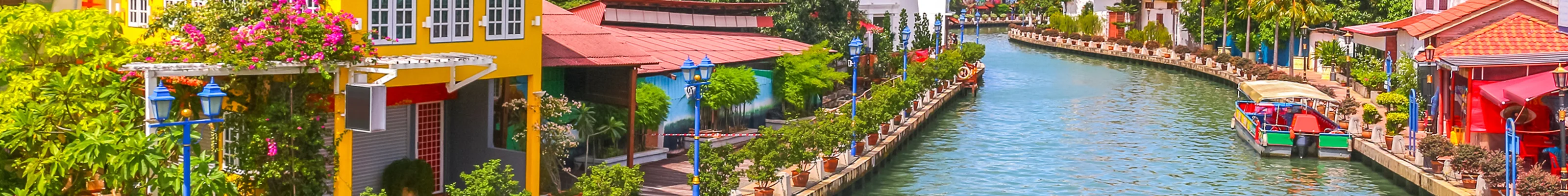 Ferry in Malacca's river next to bright and colorful buildings in Malaysia