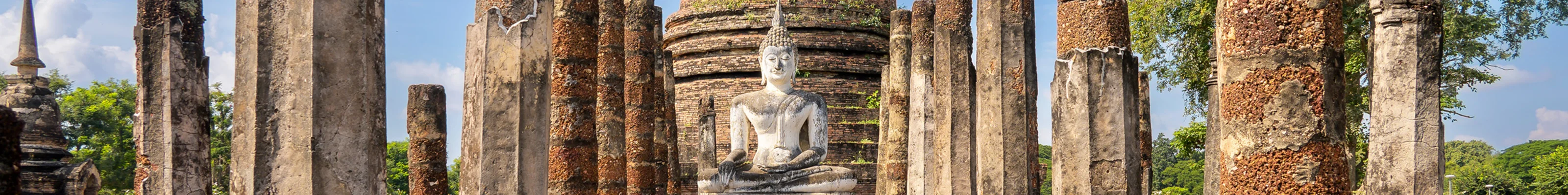 White buddha sits among stone pillars in Wat Sa Si temple in Sukhothai, Thailand