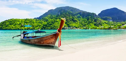Boat on beautiful white sand in Koh Phi Phi with jungle-covered mountains in the background