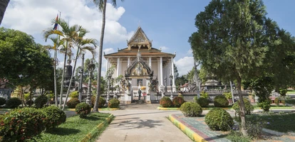 White buddhist temple with golden roof is surrounded by beautiful gardens in Battambang.
