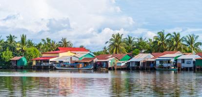 Riverside village has multi coloured houses built right on the river, with barges parked next to them and slightly clouded blue skies