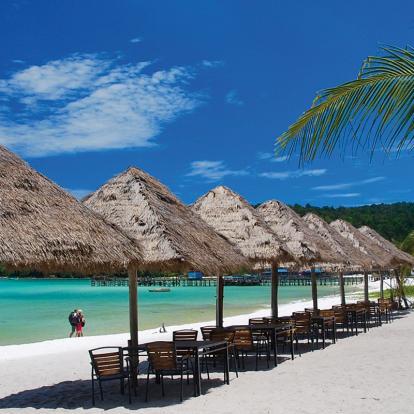 White-sand beach lined with straw-thatched umbrellas next to azure waters in Cambodia's coast.