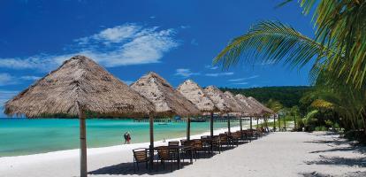 White-sand beach lined with straw-thatched umbrellas next to azure waters in Cambodia's coast.