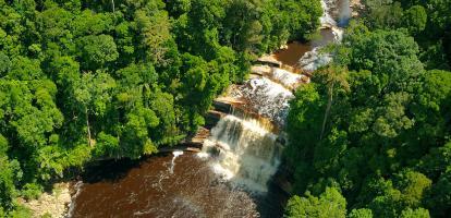 Aerial shot of waterfall and small brown lake surrounded by jungle in the Maliau Basin