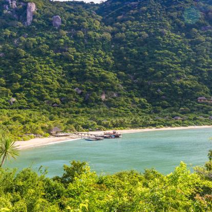 Aerial view of Ninh Van Bay, with a pier jutting out in the middle of the beach surrounded by lush mountains