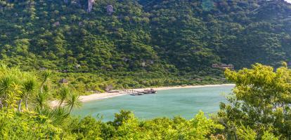 Aerial view of Ninh Van Bay, with a pier jutting out in the middle of the beach surrounded by lush mountains