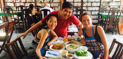 Two friends smiling with a waiter in Vietnamese restaurant