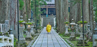 Monk in yellow clothes walking along pathway in Koya