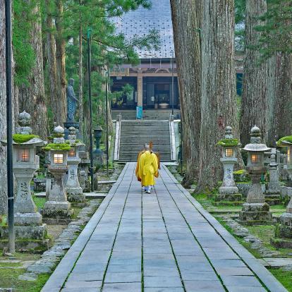 Monk in yellow clothes walking along pathway in Koya