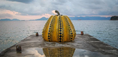 Yellow and black pumpkin sculpture on pier at Naoshima Island