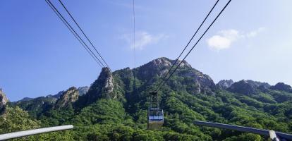 Cable car going up rocky mountains covered in tress in Seoraksan, South Korea