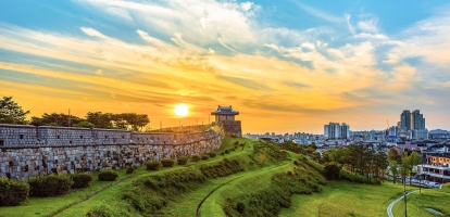 Suwon fortress walls at sunset with city skyline in background