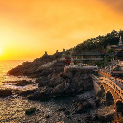 Sun setting over sea next to ornate temple and bridge in Busan