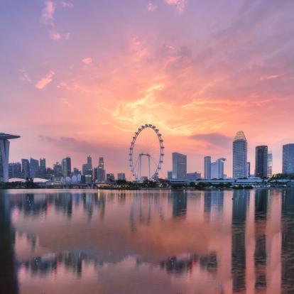 Warm and pink sky tones bath Singapore's skyline at sunset , with reflections on the water