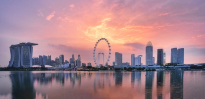 Warm and pink sky tones bath Singapore's skyline at sunset , with reflections on the water