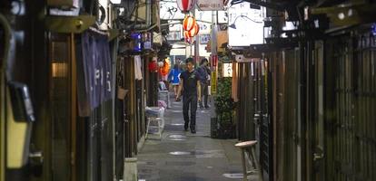 A man walks in a side street contemplating a number of different izakaya establishments in Shibuya, Tokyo