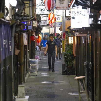 A man walks in a side street contemplating a number of different izakaya establishments in Shibuya, Tokyo
