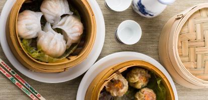 Two sets of steamed dim sum in bamboo baskets with chopsticks and dipping sauces