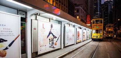 Yellow tram travelling along tracks alongside advertisements at night