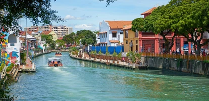 Boats with people navigate river traversing Malacca city in Malaysia