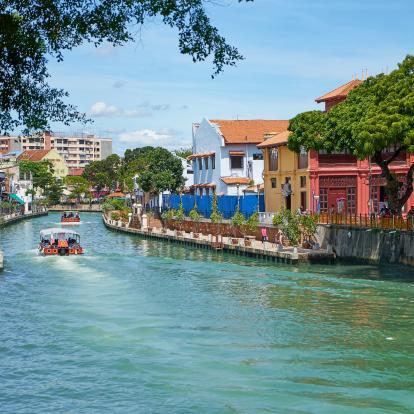 Boats with people navigate river traversing Malacca city in Malaysia