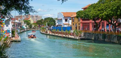 Boats with people navigate river traversing Malacca city in Malaysia