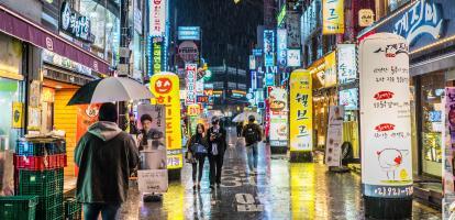 Image of a Korean city in the rain at night, with neon signs and people walkign