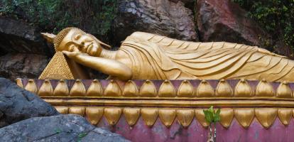 Reclining gold gilt buddha on purple platform surrounded by craggy rocks